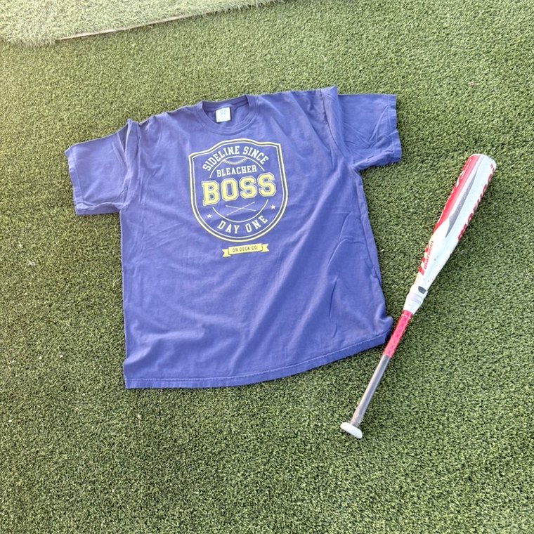 Purple Bleacher Boss tee on turf with a bat