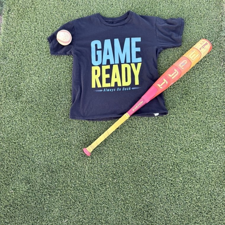 Game Ready youth tee on the field with a bat and a ball